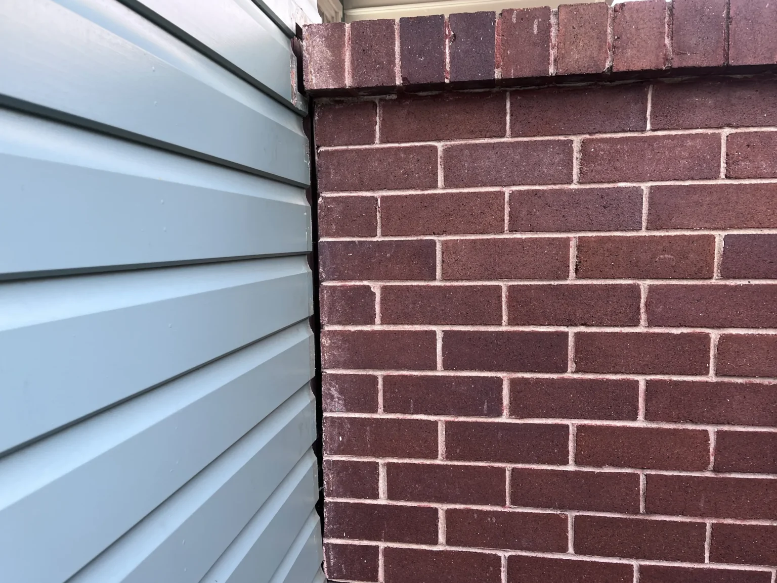 Visible gap between brick wall and siding indicating potential subsidence or foundation movement.